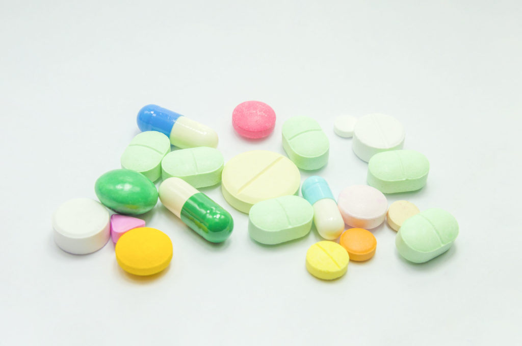 Vinte e uma pílulas médicas coloridas em todas as formas e tamanhos diferentes espalhadas em uma superfície em branco