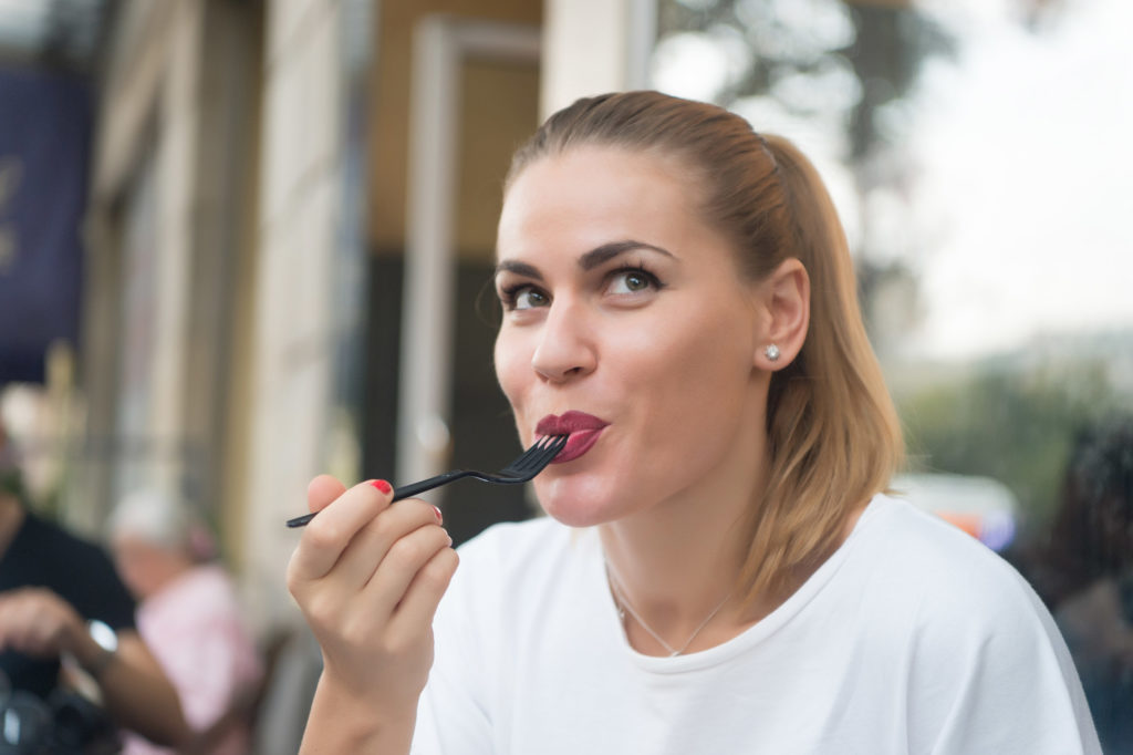 Uma mulher sentada do lado de fora sorrindo enquanto se diverte comendo com seu garfo de plástico preto