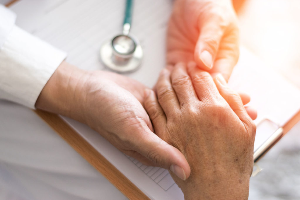 Um médico apóia a mão de um paciente com Parkinson em uma prancheta
