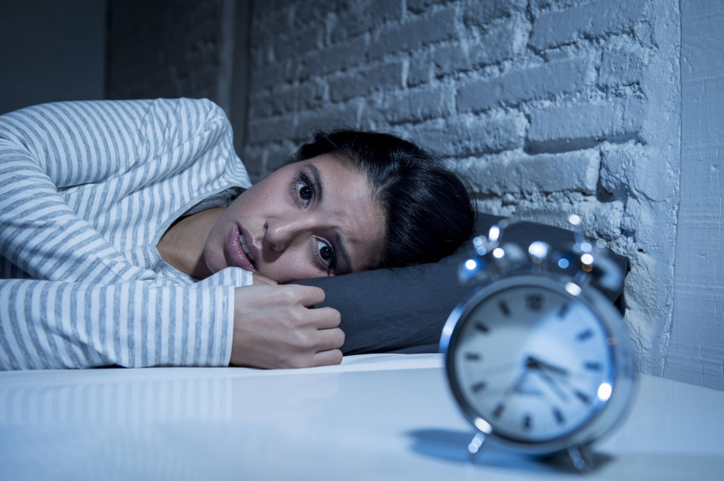 Uma mulher deitada na cama olha ansiosamente para o despertador, que marca 3h23