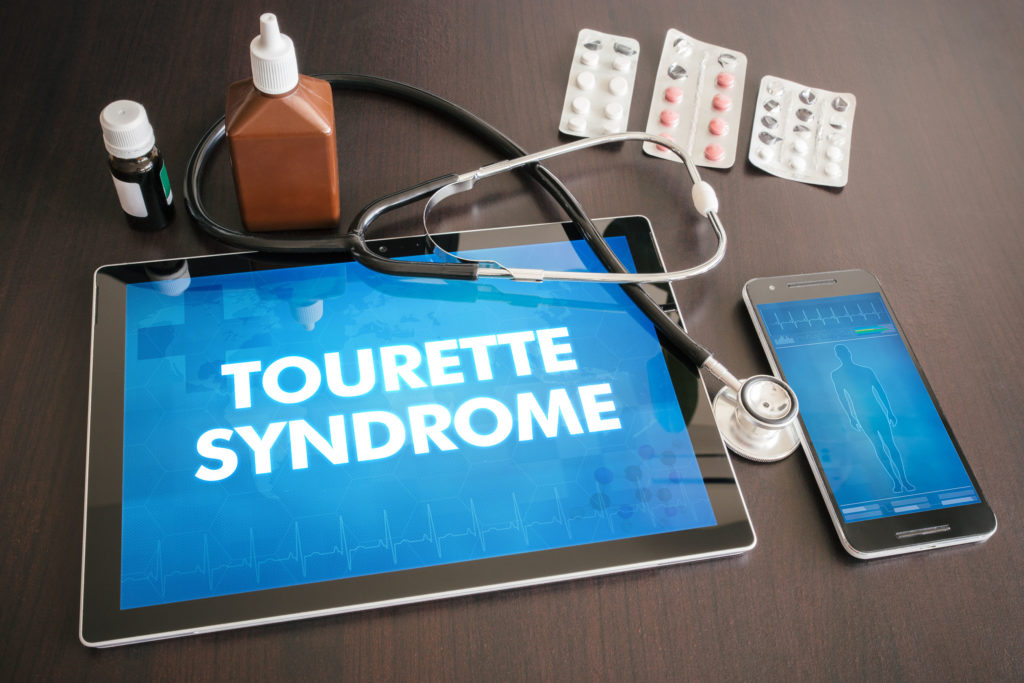 Um iPad com as palavras "síndrome de Tourette" ao lado de um iPhone, estetoscópio e medicamentos